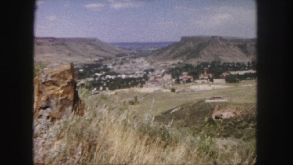 Wide 8mm view of a valley town near Denver, Colorado, framed by dry hills, rock outcrops, and distant mesas.