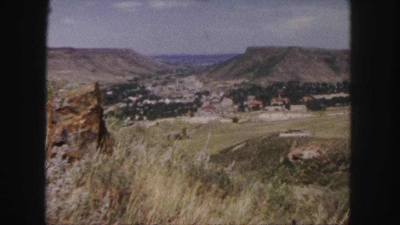 Small town in a valley seen from a grassy rocky overlook.