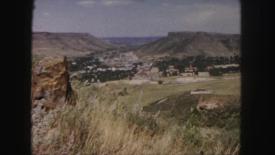 1958 Colorado home-movie frame showing a small town across open fields beneath rugged hills.
