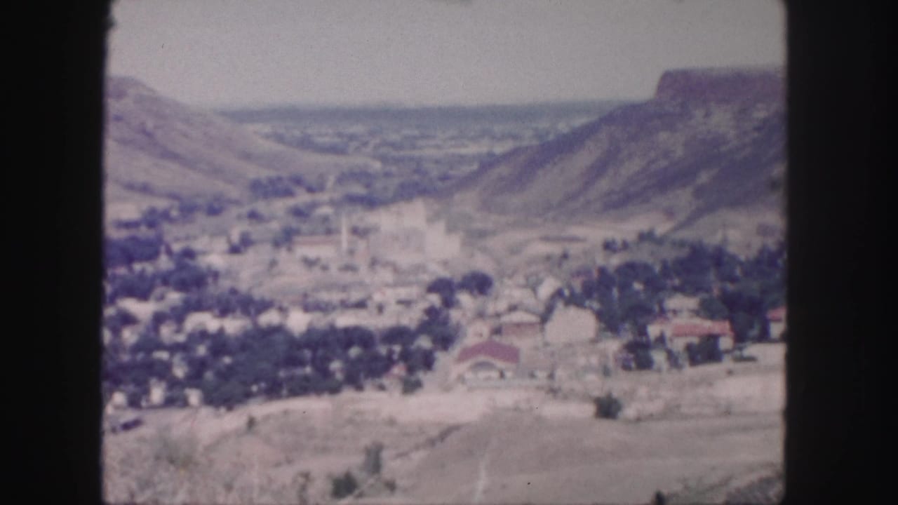 Soft distant view of a valley town between hills and rugged mountain slopes.