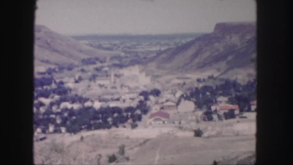 1958 8mm view near Denver showing a hazy valley town, open hills, rooftops, roads, and surrounding mountain slopes.