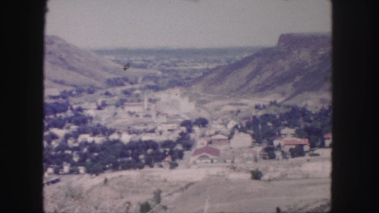 1958 Colorado home-movie frame with a broad valley settlement viewed from an elevated overlook near Denver.