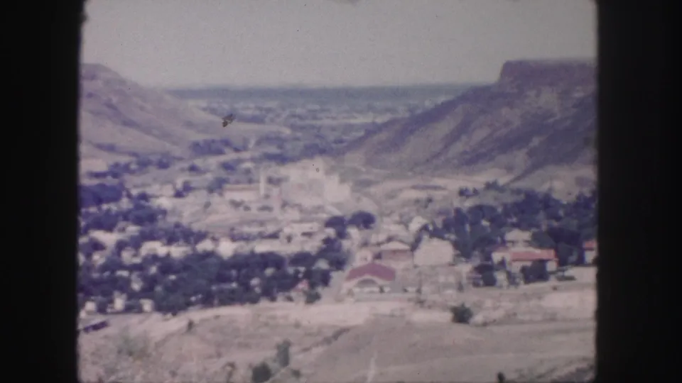 1958 Colorado home-movie frame with a broad valley settlement viewed from an elevated overlook near Denver.