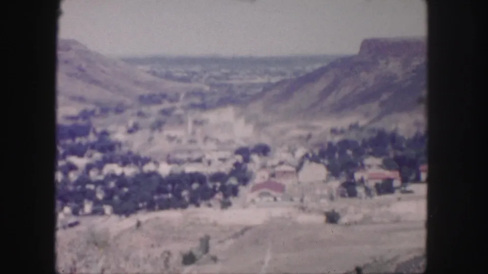 1958 8mm panorama near Denver showing a small town spread across a valley floor beneath rugged hills.