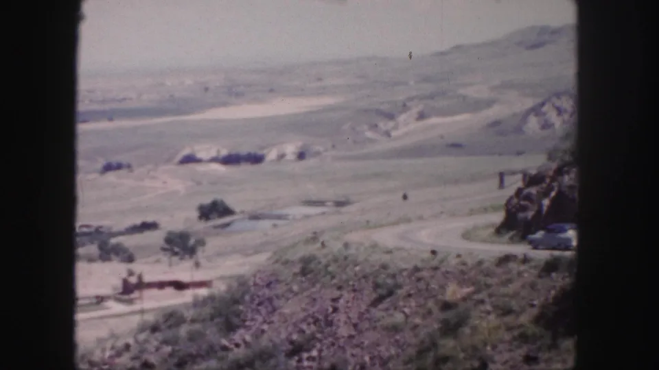 A faded 8mm frame near Denver shows a curving road through dry hills, with rocky foreground and open valley beyond.