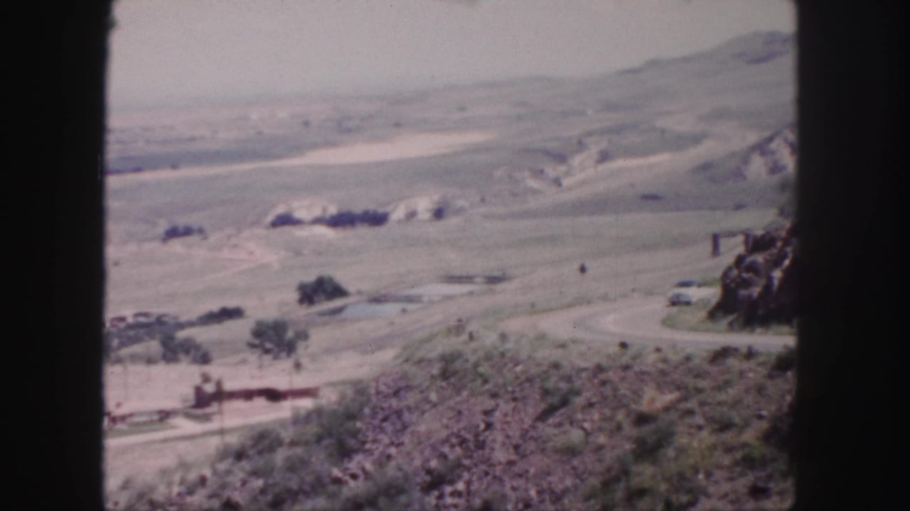 1958 Colorado travel footage showing a white car on a curving road amid arid terrain and distant hills near Denver.
