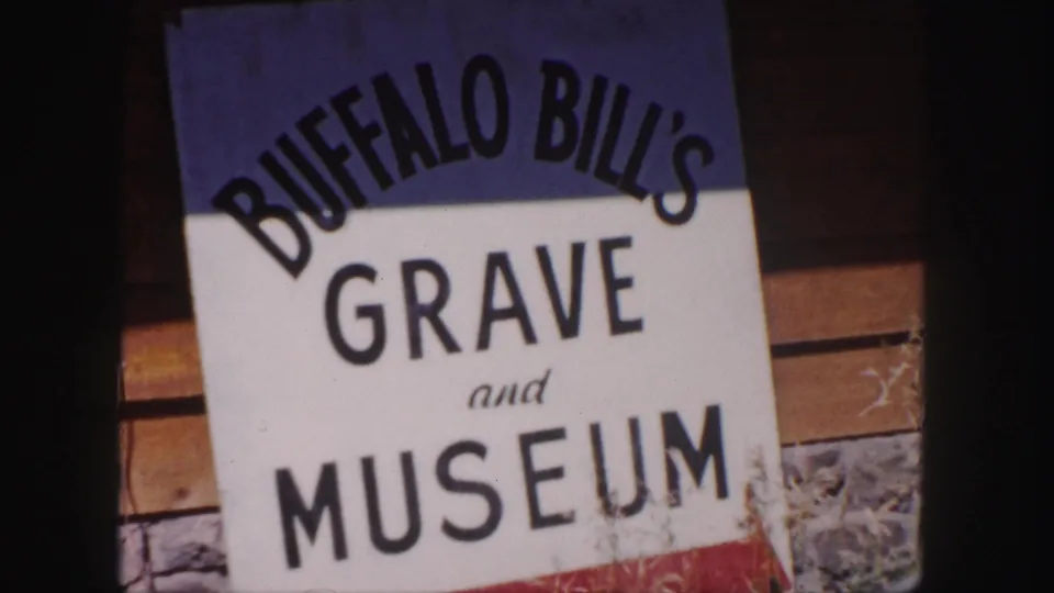 1958 Denver-area 8mm frame showing a readable Buffalo Bill's Grave and Museum sign beside a rustic wall.