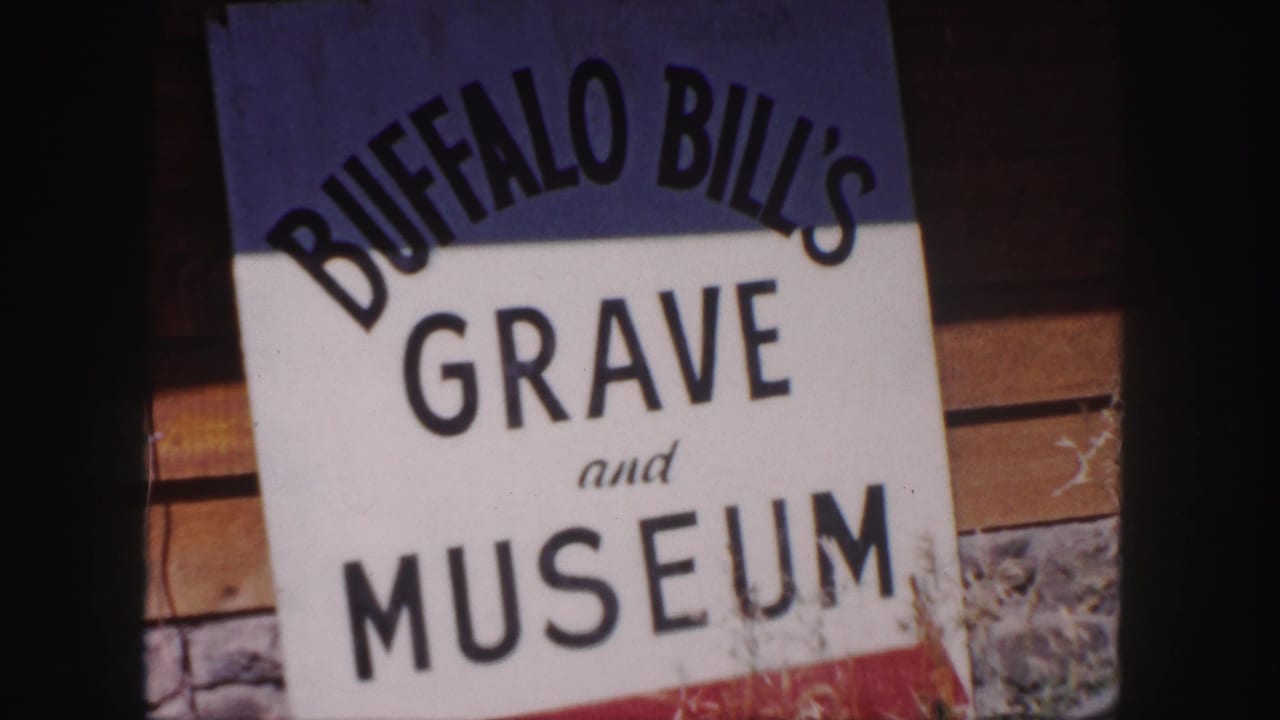 Close 8mm frame of the Buffalo Bill's Grave and Museum sign, with large black lettering and wood-and-stone building details behind it.