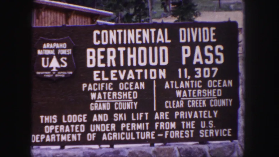 1958 Colorado home-movie still of the Berthoud Pass sign, including county and watershed text on the Continental Divide marker.