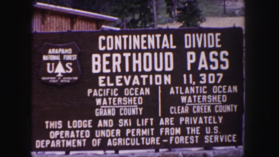 Final 8mm frame of the Berthoud Pass sign, with permit wording and watershed labels visible on the board.
