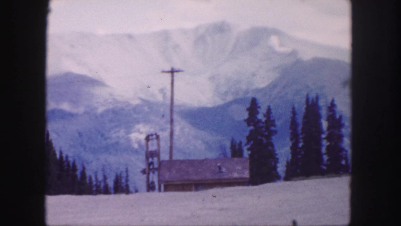 1958 Colorado mountain view near Berthoud Pass, showing snowy slopes, evergreens, a small lodge roof, a utility pole, and ski-lift structure.