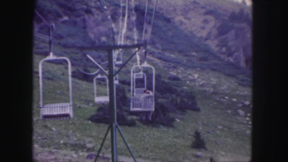 1958 Colorado 8mm frame showing open ski-lift chairs, cables, a lift tower, and a rocky green mountain slope.