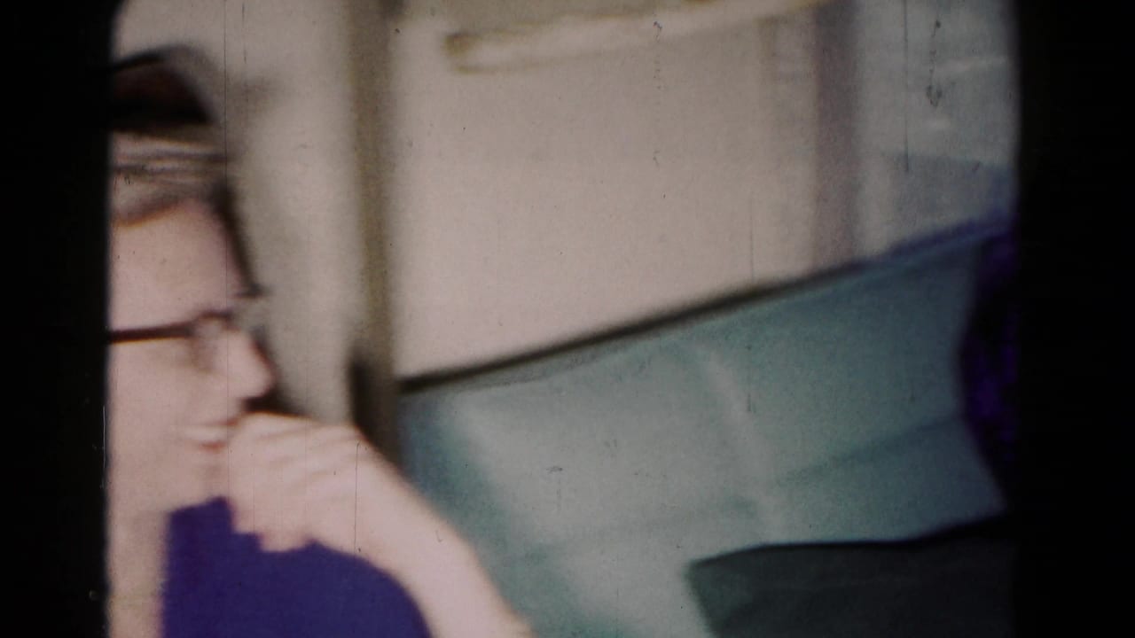 A blurred woman with glasses sits near a sofa back in a home interior.