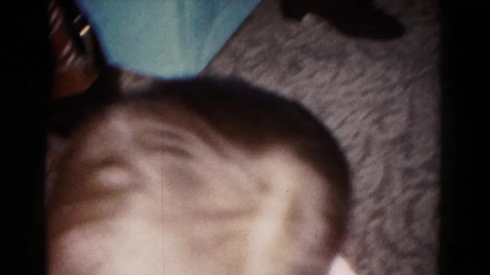 The frame catches a cropped foreground head with the sofa, carpet, and part of the room visible in the 1958 Hagerstown interior.