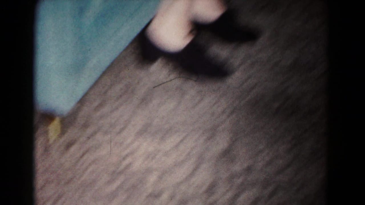 Handheld view of a wooden floor with a blurred figure partly entering the frame.