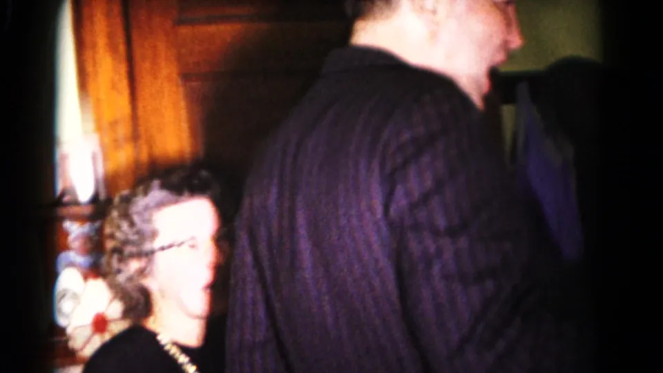 A smiling woman with glasses appears beside a tall man in a dark striped shirt during the 1958 Hagerstown indoor gathering.