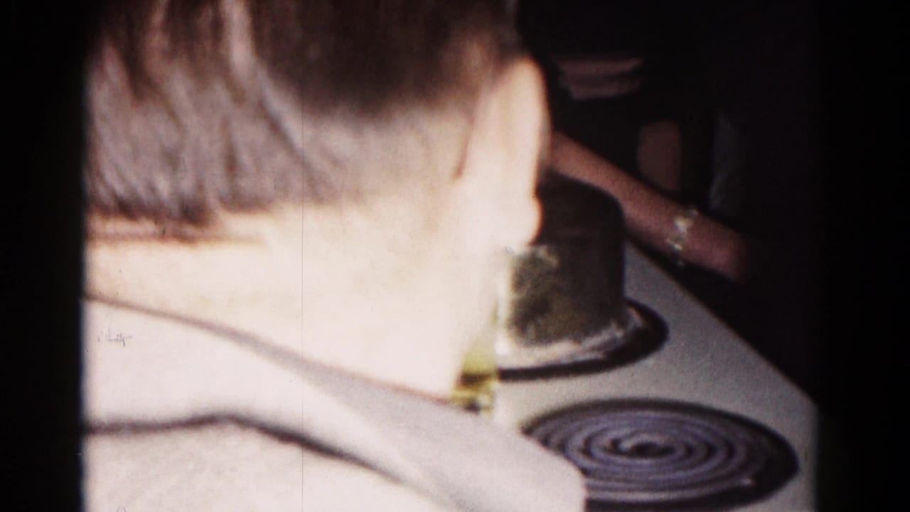Man seen from behind near a kitchen stove during an indoor gathering.
