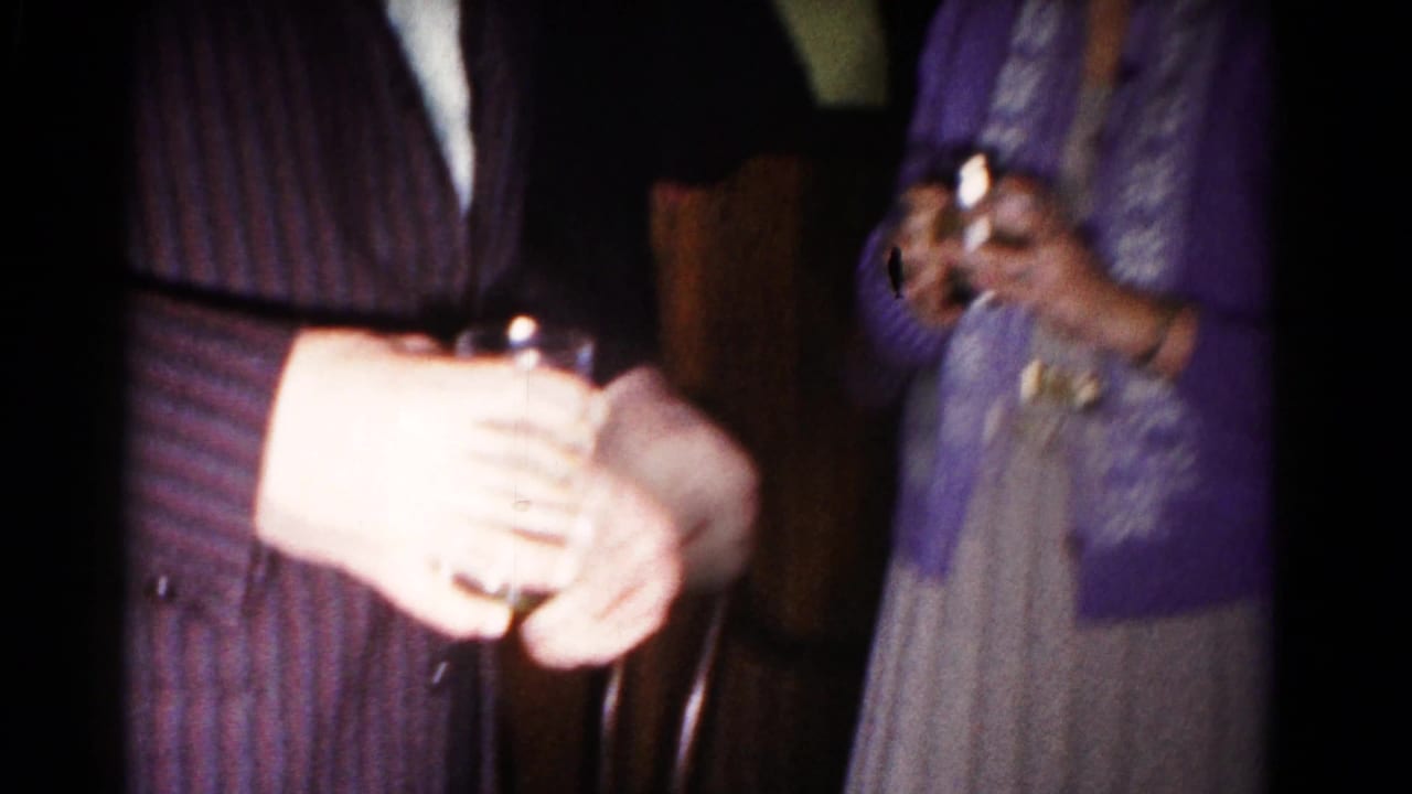 Adults at a 1958 Hagerstown kitchen party stand close together, with one man in a striped suit holding a drink and a woman nearby.