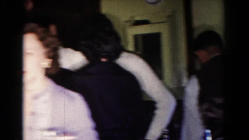 A candid 1958 Hagerstown home-movie frame shows adults passing through a crowded kitchen, with faces partly blurred by motion and exposure.