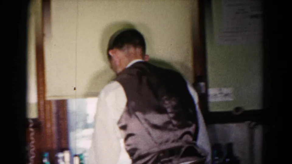 A man in a vest walks past a doorway in the 1958 Hagerstown kitchen party footage, with bottles or glasses low in the frame.