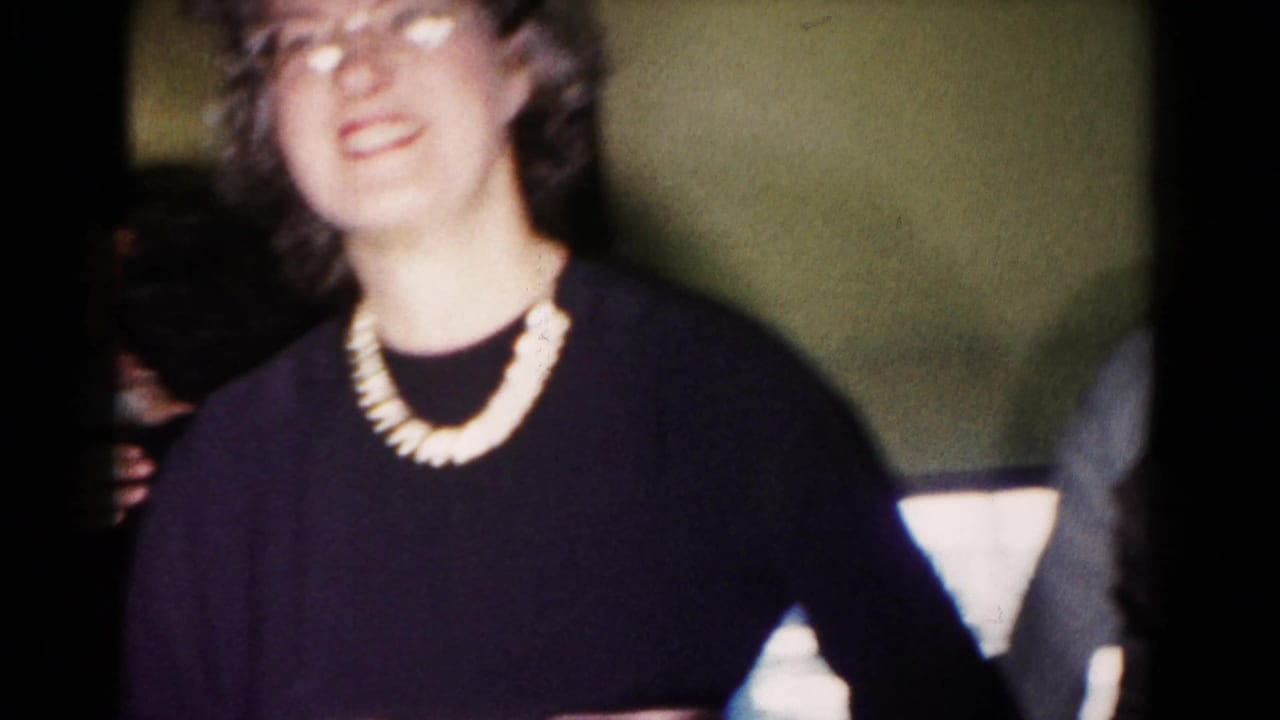 Woman with glasses and a white necklace smiling close to the camera.