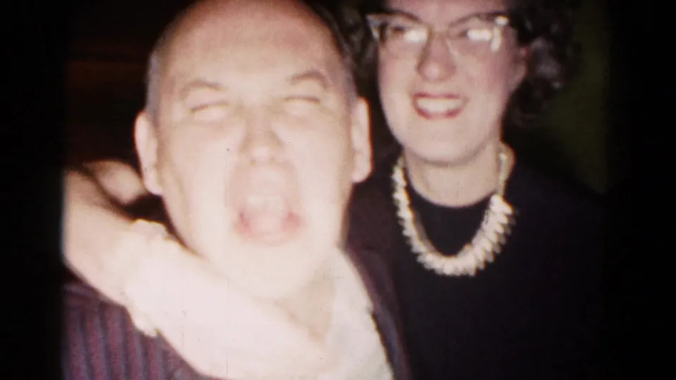1958 Hagerstown party frame with a bald man pulling a face as a woman in glasses smiles behind him.