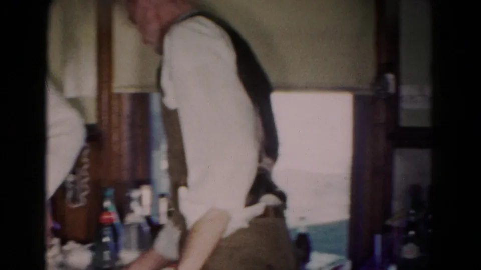 1958 Hagerstown indoor scene with a vest-wearing man beside bottles and bar items in a private interior.