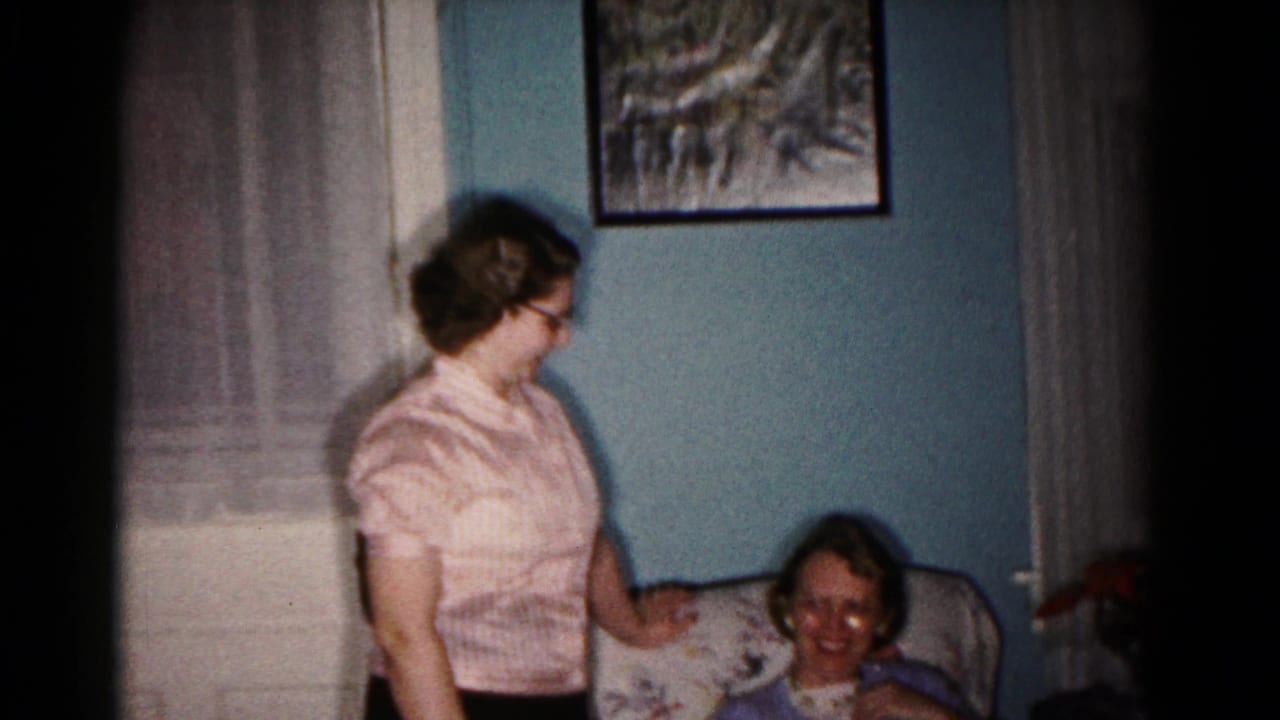 Standing woman looks toward a seated woman smiling in an upholstered chair.