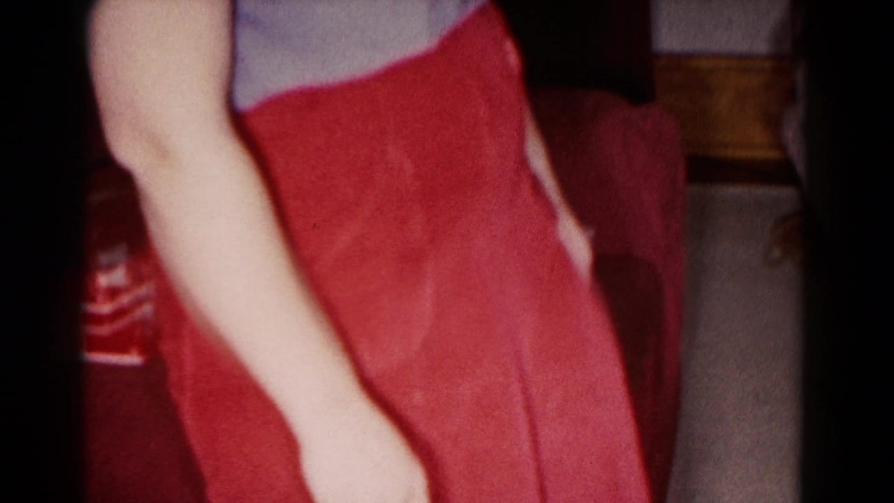 Close cropped view of a person in a red skirt with an arm at side near a chair and curtain.