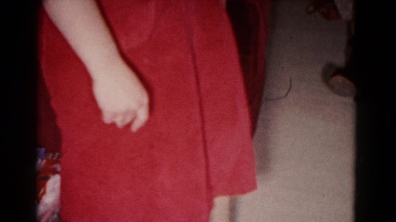 1958 Hagerstown home-movie frame showing a standing person in a blue shirt and red skirt, cropped by the handheld camera.