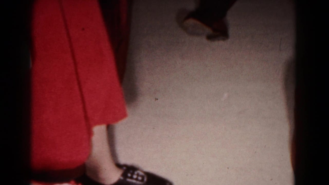 1958 Hagerstown interior frame focused on the lower part of a standing person in a red skirt and dark shoes on carpet.