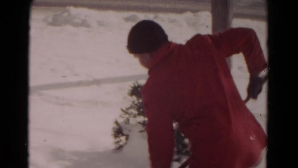 The red-coated person leans forward with a shovel while clearing snow in the 1958 Hagerstown winter scene.