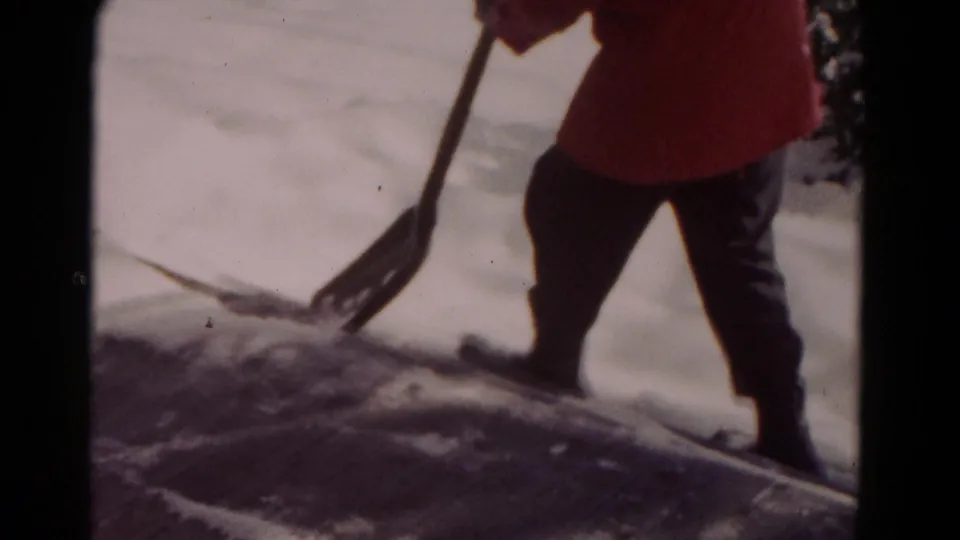 The person stands with a shovel at the edge of a cleared patch of snow, with dark boots and winter clothing visible in the 1958 scene.