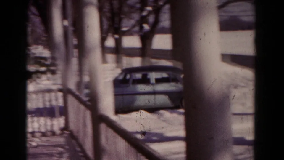 The sedan is seen from behind near snowy ground and porch columns, with residential framing in the foreground.