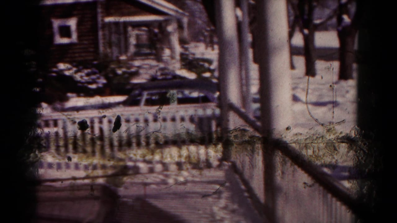 Snowy porch view with white railings, a blue car, houses, and winter ground cover.