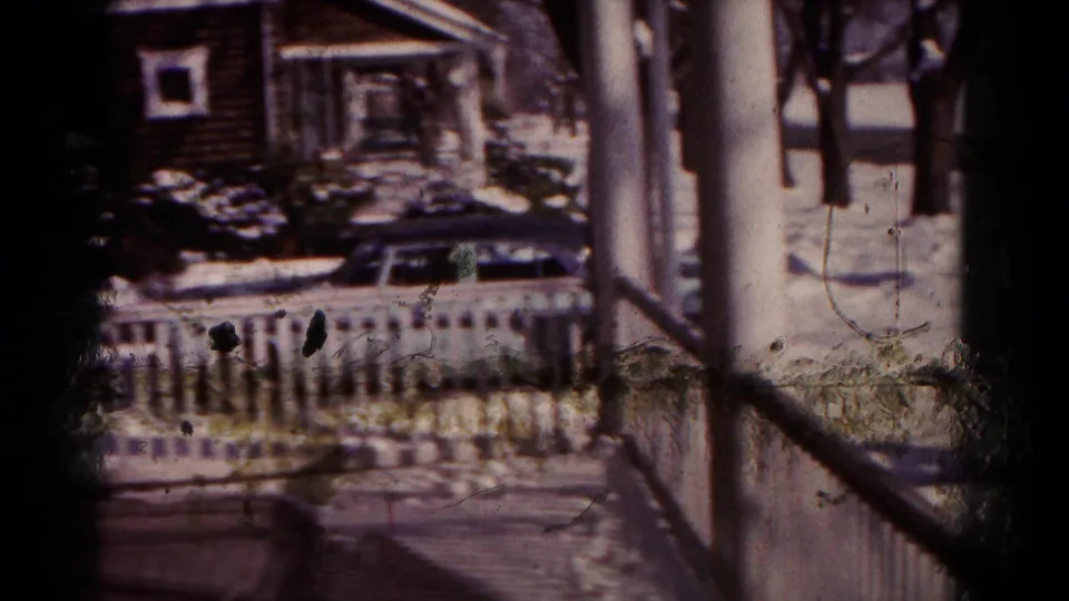 1958 Hagerstown home-movie frame looking from a porch toward a snow-covered driveway, blue car, white railing, and neighboring houses.