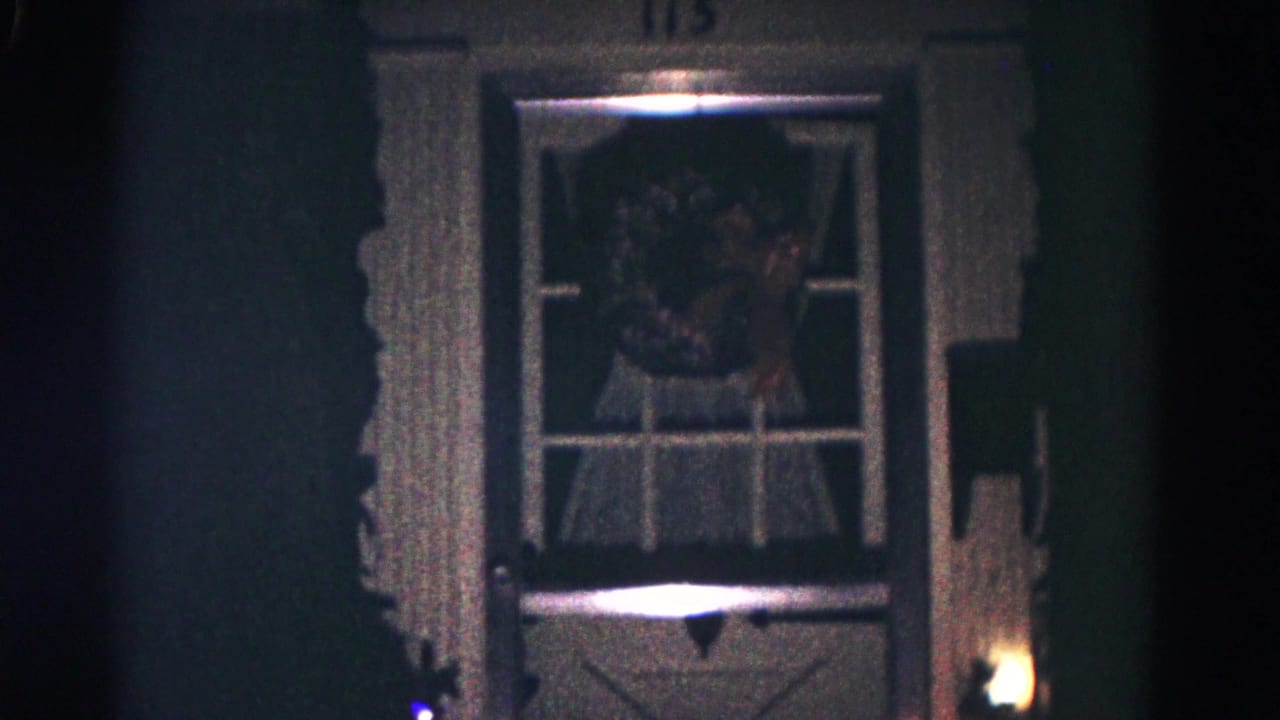 Nighttime 1958 Hagerstown frame showing a front door window with a Christmas wreath, curtains, trim, and dim exterior light.