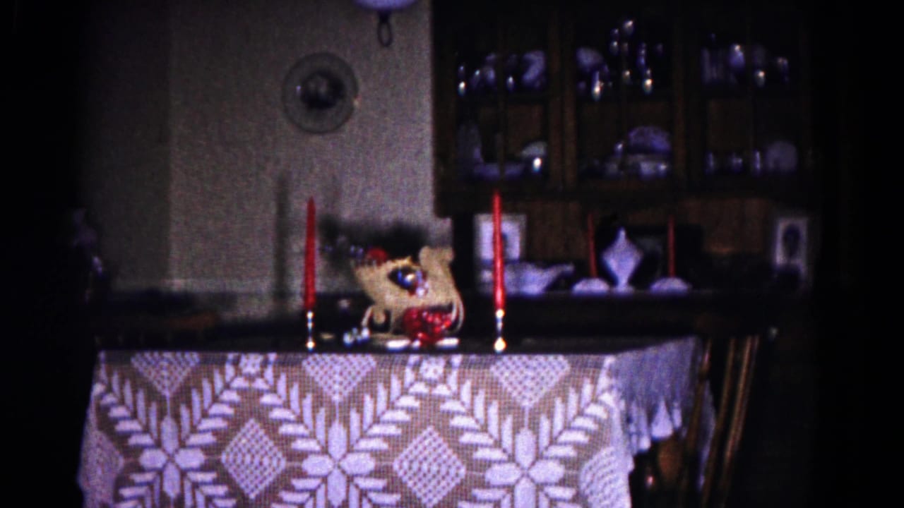 Candlelit dining table with patterned cloth and china cabinet in a dim room.