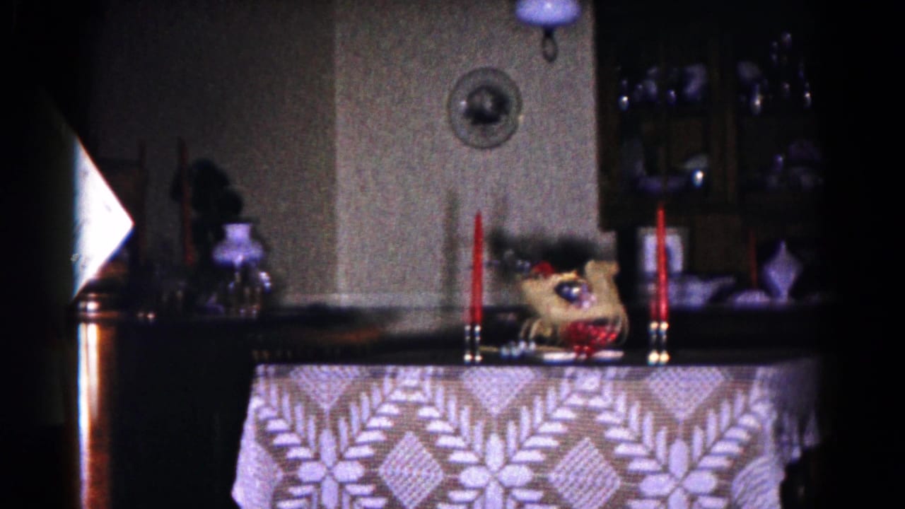 1958 Hagerstown home-movie frame showing a Christmas tabletop arrangement with red candles, lace cloth, and shelves in a private interior.