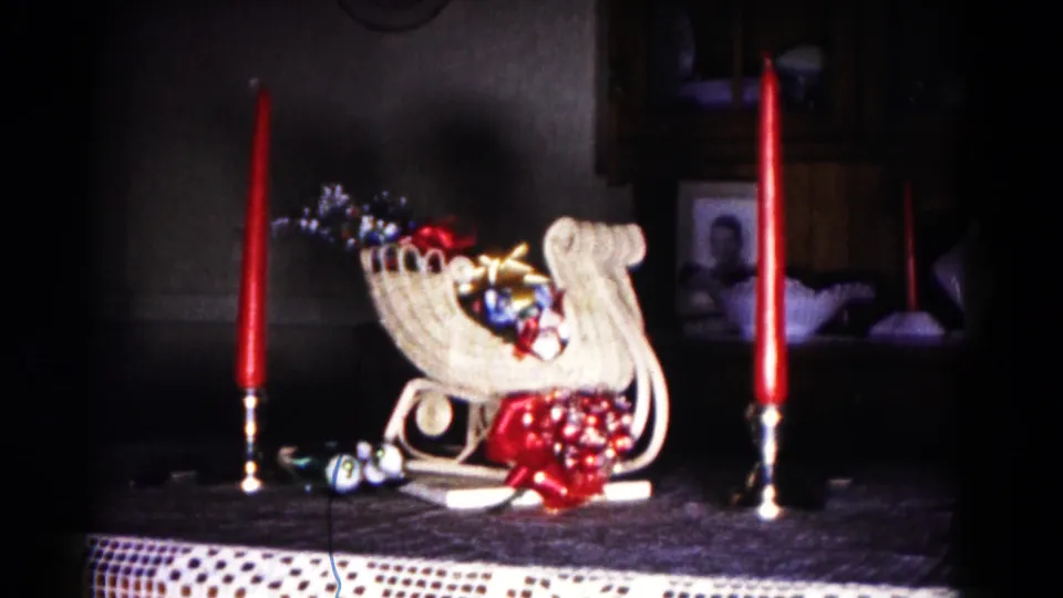 1958 Hagerstown home-movie still showing a Christmas sleigh centerpiece with ornaments, red bow, and tall red candles.