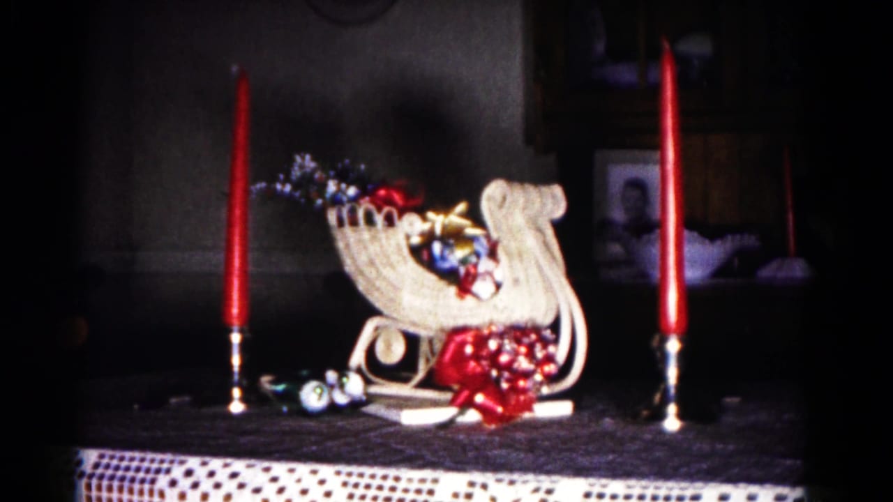 Miniature white sleigh with ornaments on a table between two red candles.