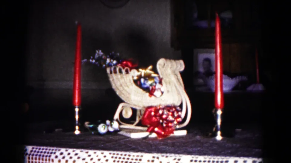 1958 Hagerstown home-movie frame showing a tabletop holiday sleigh with ornaments, red taper candles, and dim interior decor.
