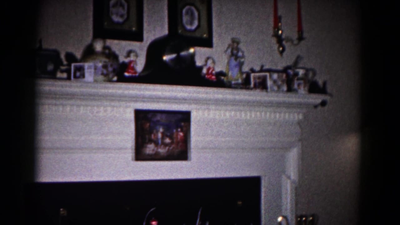 1958 Hagerstown home-movie frame showing a white fireplace mantel with framed photos, small figurines, and a dark hearth.
