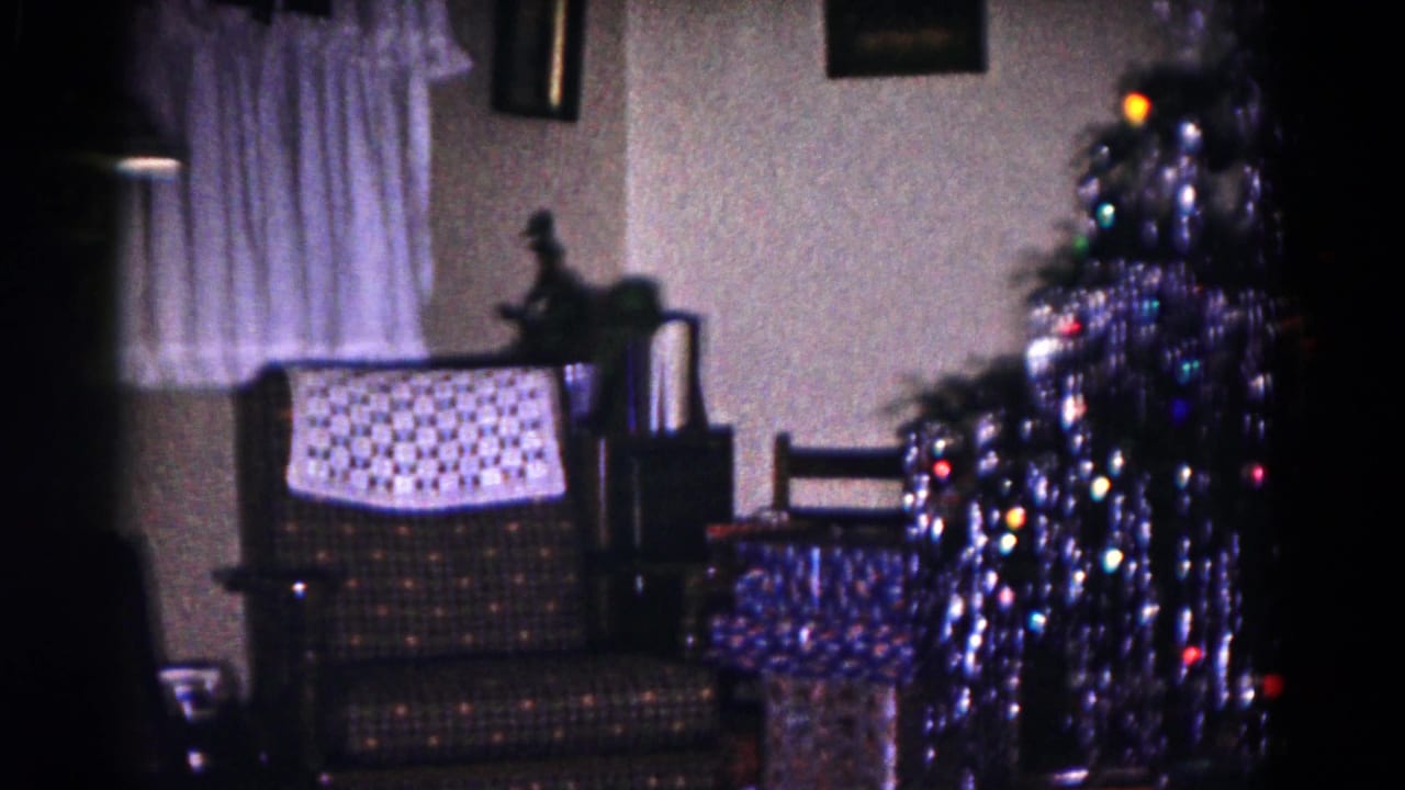 Decorated Christmas tree with tinsel beside a patterned armchair and wrapped presents.