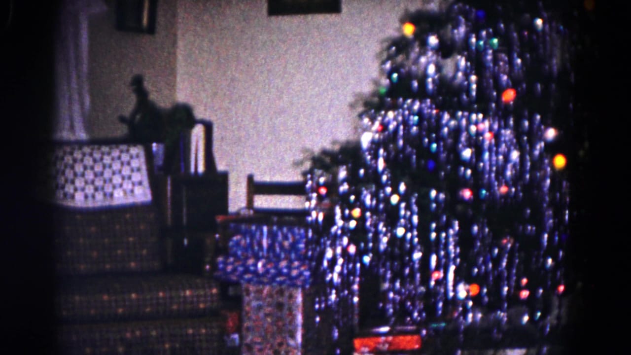 Tinsel-covered Christmas tree with colored lights and presents in a living room.