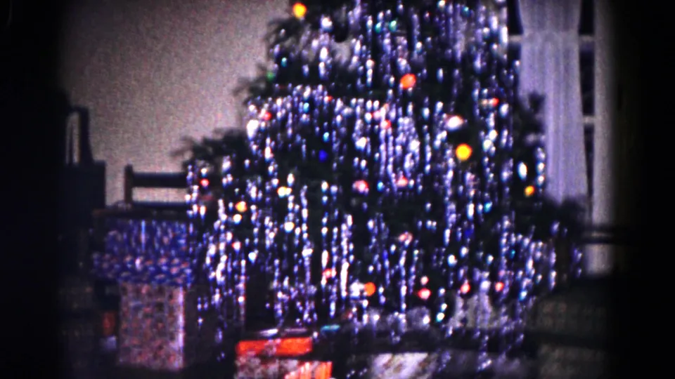 1958 Hagerstown home interior showing the Christmas tree filling the frame, with lights, tinsel, wrapped presents, curtains, and nearby seating.