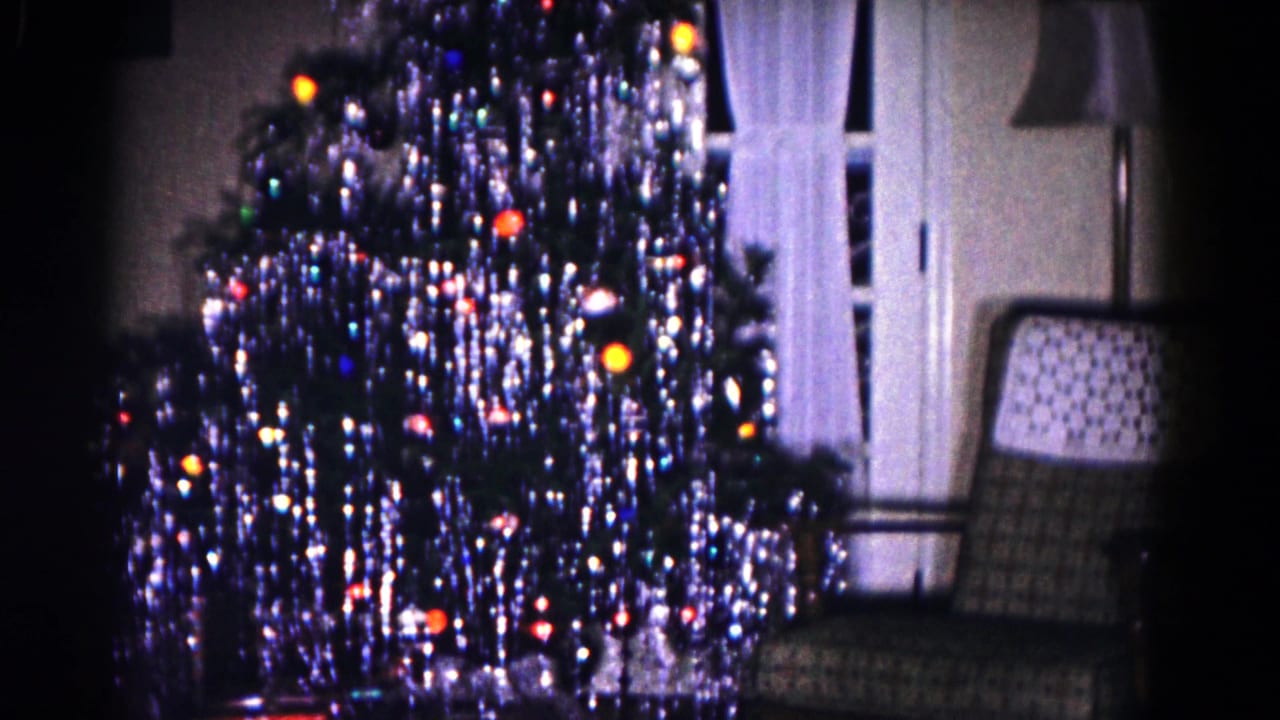 1958 Hagerstown home-movie frame showing a decorated Christmas tree with tinsel, colored lights, curtains, and a patterned armchair.