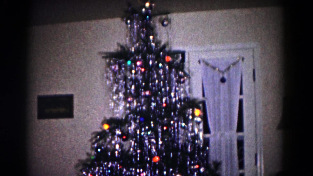 1958 Hagerstown home-movie frame showing a tinsel-covered Christmas tree near a white door in a dim interior.