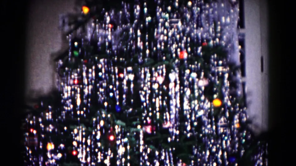 1958 home-movie frame of the lower decorated Christmas tree, with tinsel and colored lights filling the view.