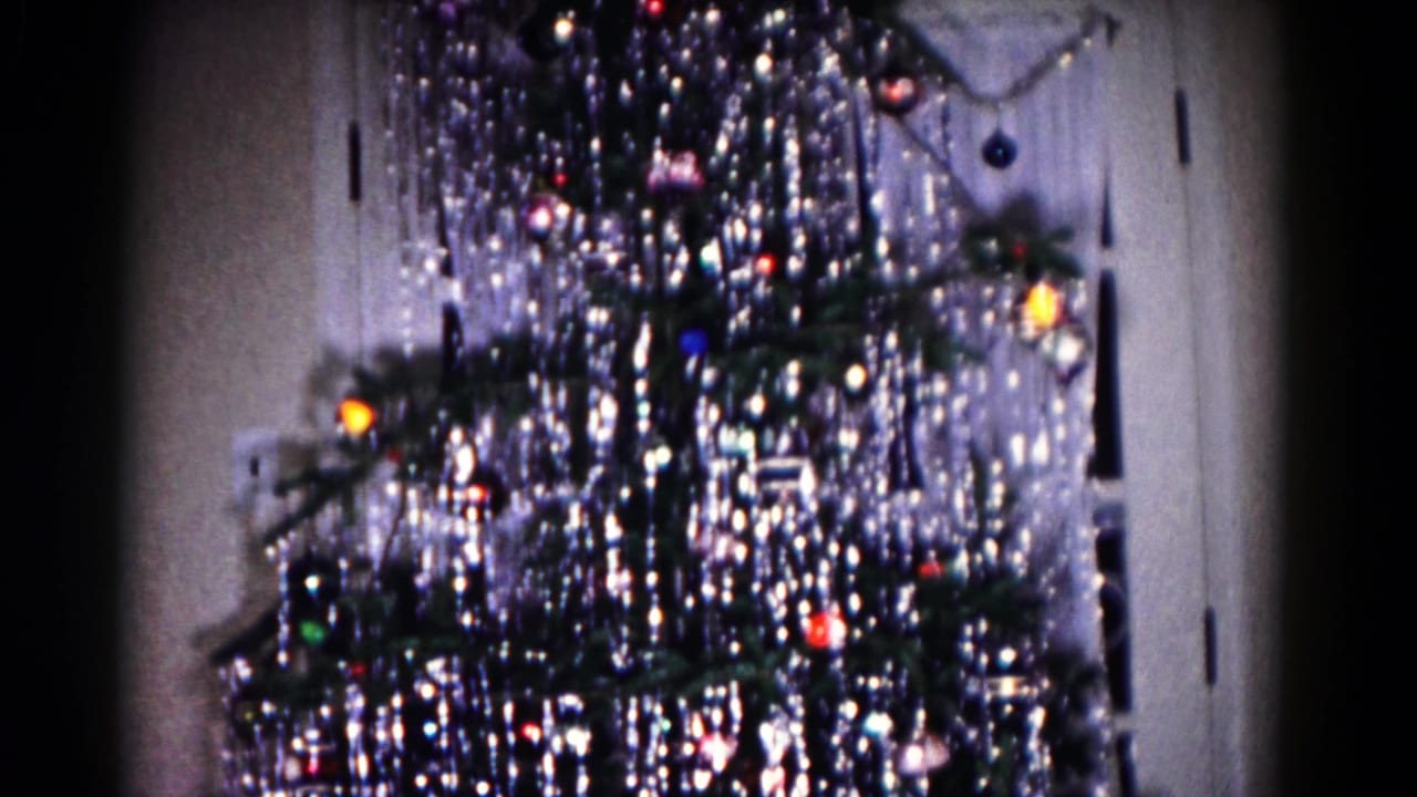The Christmas tree remains framed indoors, showing dense silver tinsel, dark branches, colored bulbs, ornaments, and a door at the right.